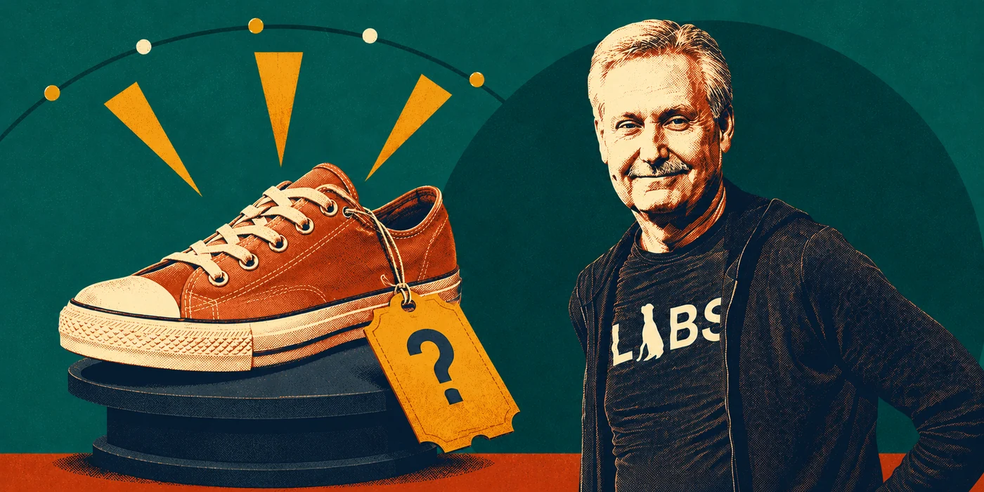 A terracotta sneaker on a dark stepped pedestal under a string of fairground bulbs, a ticket shaped price tag with a question mark hanging from its laces, and Gary Keller standing beside it